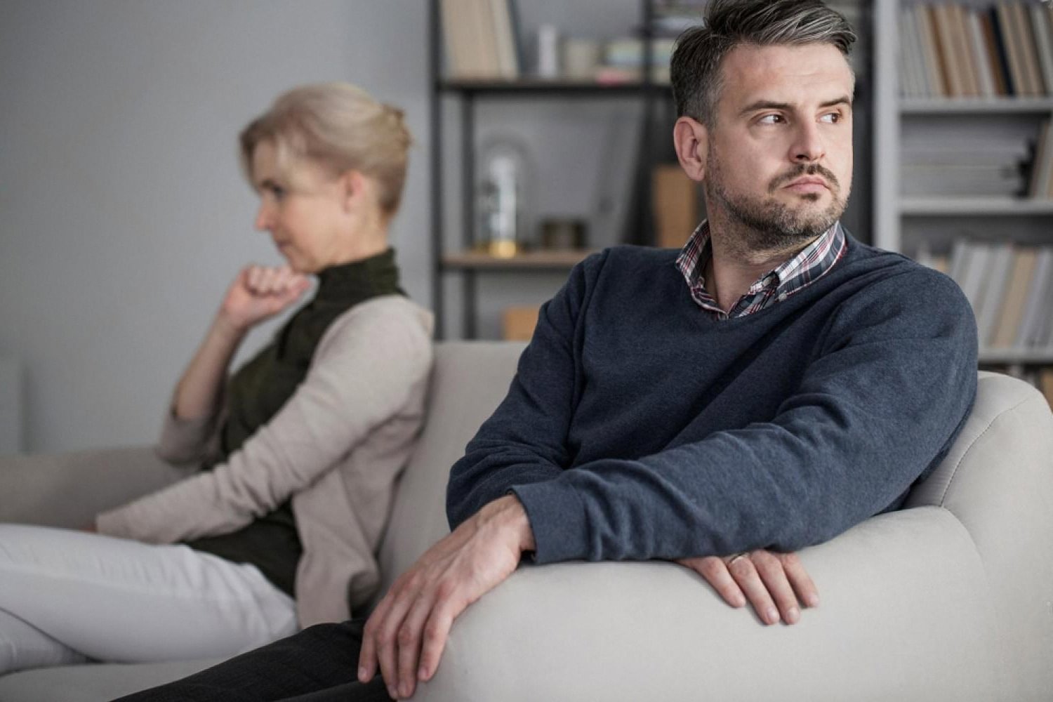 Expat couple sitting apart on a sofa during a difficult conversation about divorce in Dubai
